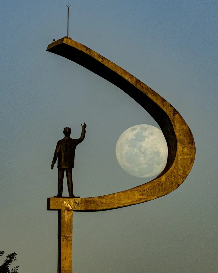 Lua e estátua de JK enquadradas dentro do arco do monumento.